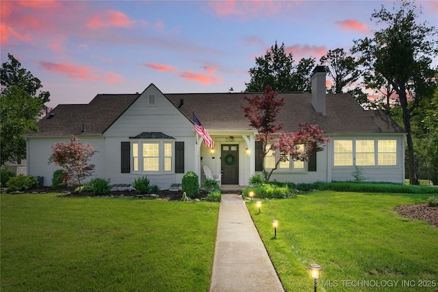 view of front of home with a chimney, a lawn, and a shingled roof