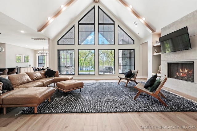 living area with wood finished floors, a chandelier, a high end fireplace, beamed ceiling, and high vaulted ceiling