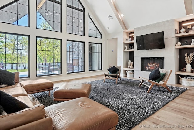 living area with wood finished floors, high vaulted ceiling, built in features, beam ceiling, and a tile fireplace