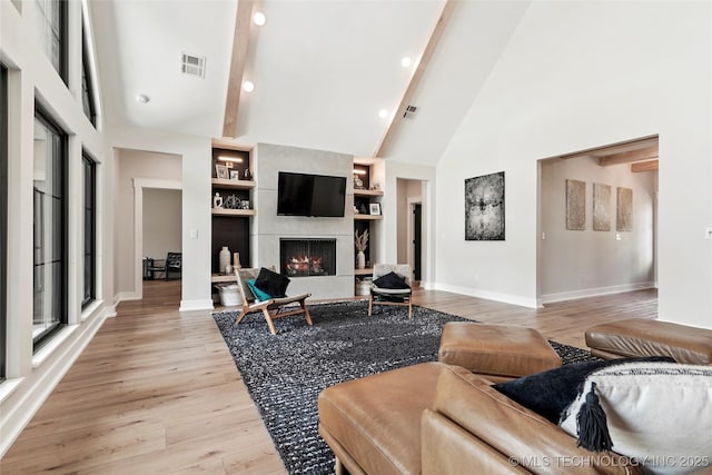 living area featuring baseboards, light wood-style floors, beamed ceiling, high vaulted ceiling, and a fireplace