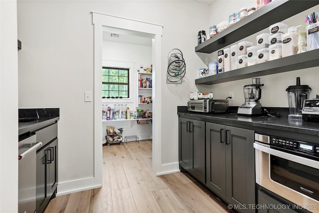 bar area featuring light wood-style floors, stainless steel oven, and baseboards
