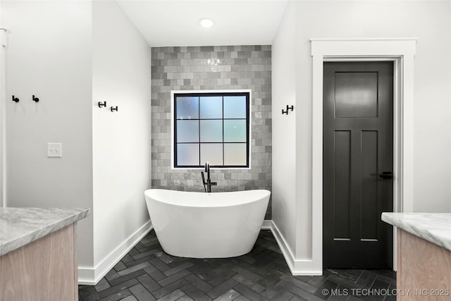 bathroom with a freestanding tub, baseboards, tile walls, and vanity