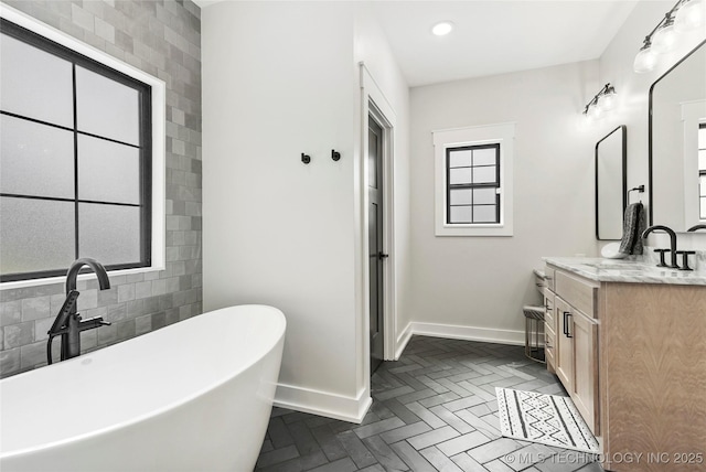 full bath featuring baseboards, vanity, a freestanding tub, and recessed lighting