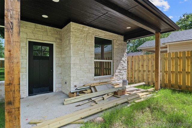 entrance to property with stone siding, fence, and roof with shingles