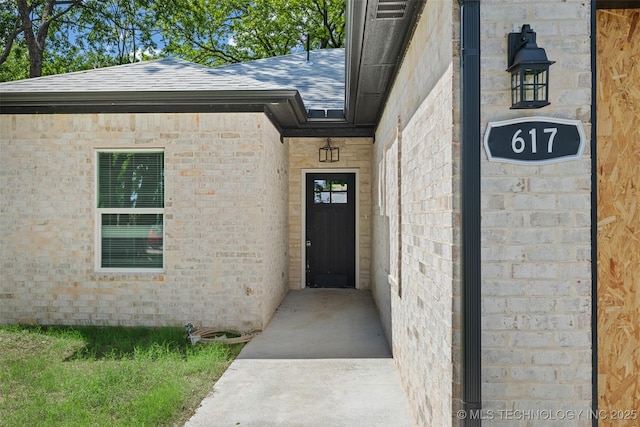 entrance to property with roof with shingles and brick siding