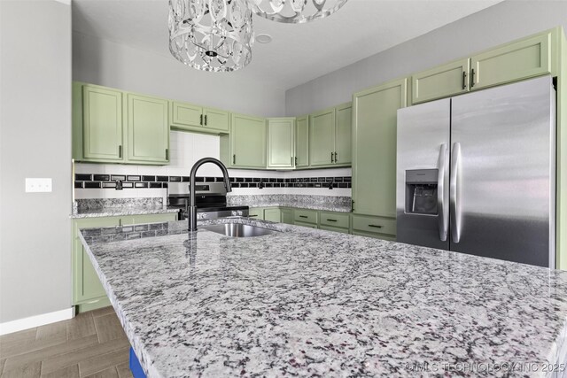 kitchen featuring stainless steel fridge, green cabinets, a sink, a chandelier, and light stone countertops