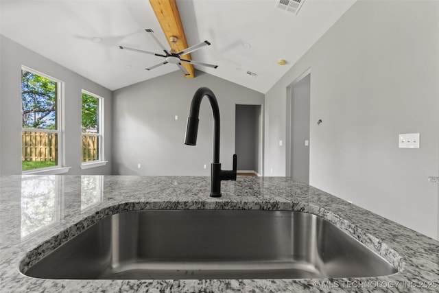 kitchen view of a sink, beam ceiling, ceiling fan, and light stone counters