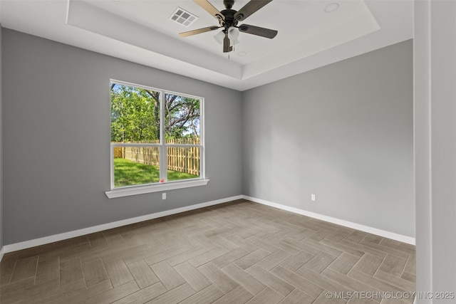 spare room featuring a raised ceiling, baseboards, and ceiling fan