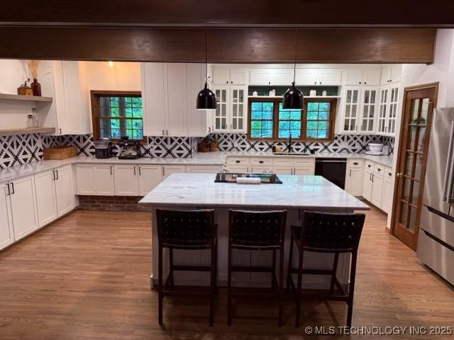 15373 N Javine Hill Rd, Skiatook, OK 74070 - kitchen with black dishwasher, freestanding refrigerator, wood finished floors, a kitchen breakfast bar, and decorative backsplash