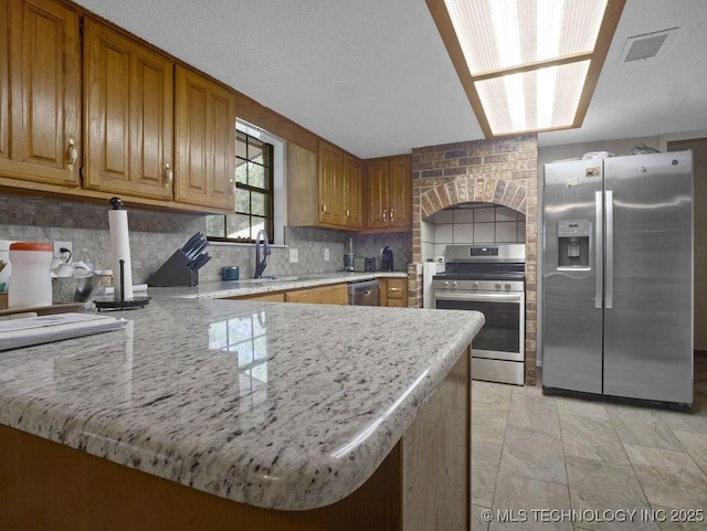 311 Washington Ave, Boswell, OK 74727 - kitchen featuring stainless steel appliances, a sink, decorative backsplash, a peninsula, and brown cabinetry