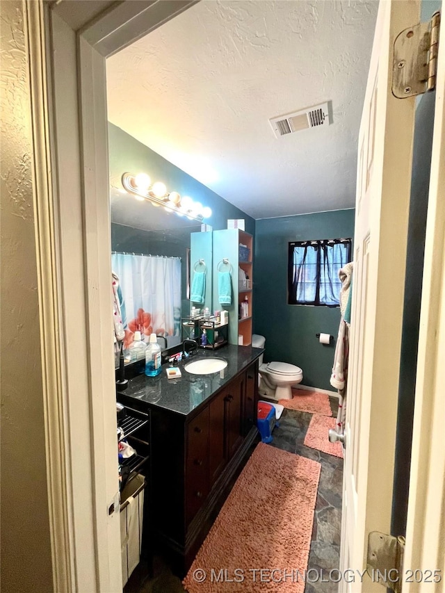 1715 Worley, Durant, OK 74701 - bathroom with stone finish floors, toilet, vanity, and a textured ceiling