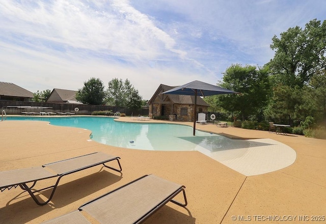 community pool with a patio, fence, and an outbuilding