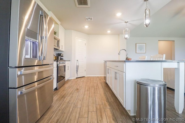 kitchen with appliances with stainless steel finishes, light wood-style floors, white cabinets, a sink, and pendant lighting