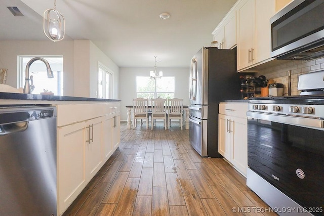 kitchen with appliances with stainless steel finishes, dark wood-style flooring, white cabinets, a chandelier, and decorative backsplash