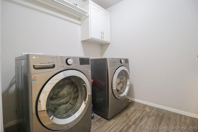 clothes washing area with washer and clothes dryer, cabinet space, light wood-type flooring, and baseboards