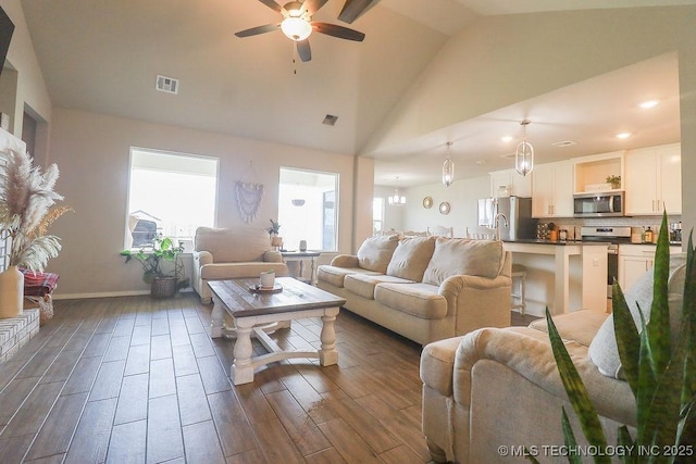 living room featuring vaulted ceiling, plenty of natural light, a ceiling fan, dark wood finished floors, and baseboards
