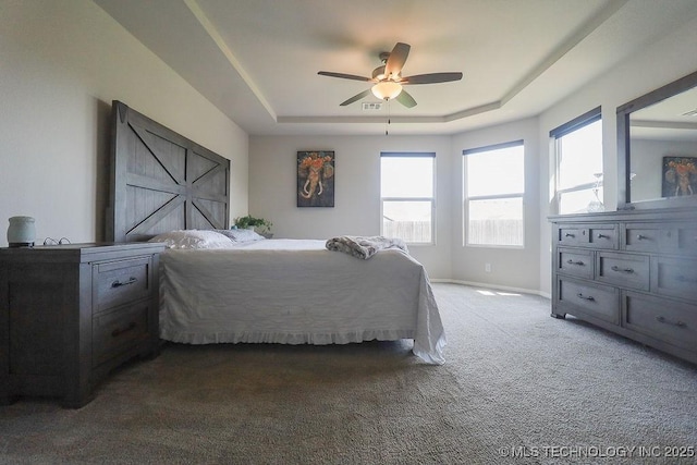 carpeted bedroom with a raised ceiling, multiple windows, a ceiling fan, and baseboards