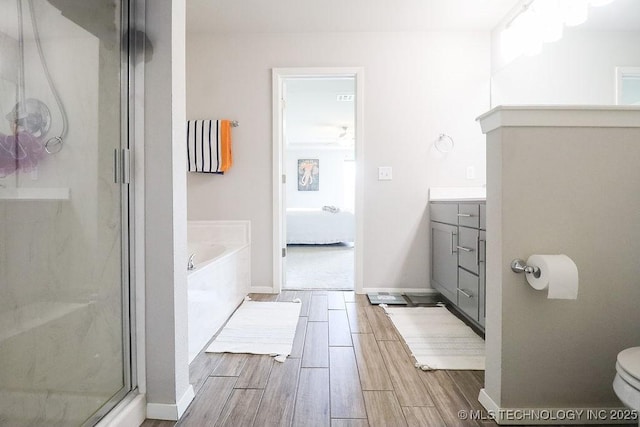 full bath featuring a stall shower, wood finished floors, a garden tub, toilet, and baseboards