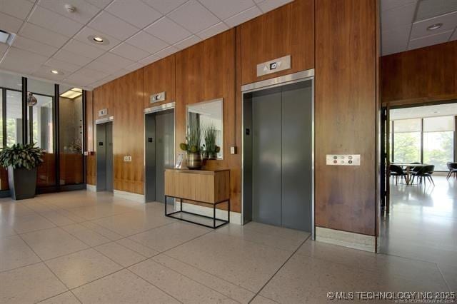 community lobby with wood walls, a drop ceiling, and a towering ceiling