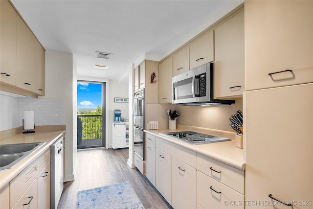 kitchen featuring appliances with stainless steel finishes, light wood-type flooring, light countertops, cream cabinetry, and backsplash