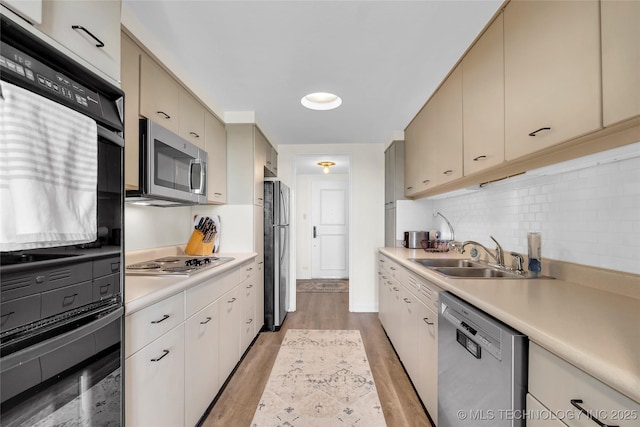 kitchen featuring appliances with stainless steel finishes, a sink, light countertops, light wood-style flooring, and backsplash