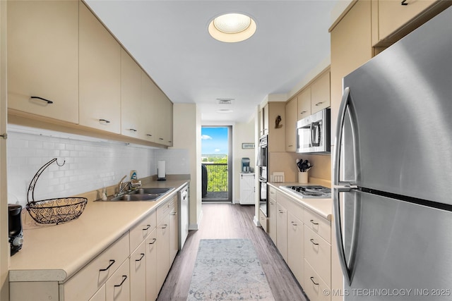 kitchen with appliances with stainless steel finishes, a sink, light wood-type flooring, and light countertops