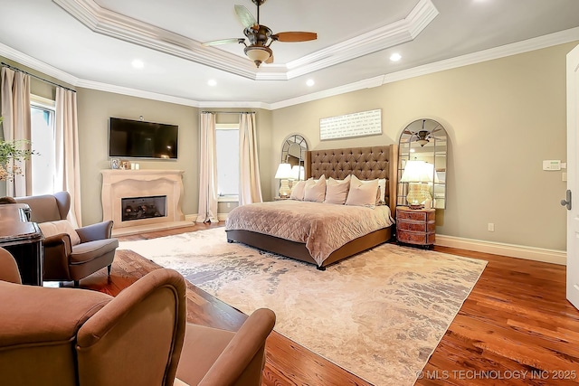 bedroom with ornamental molding, wood finished floors, baseboards, a raised ceiling, and a fireplace