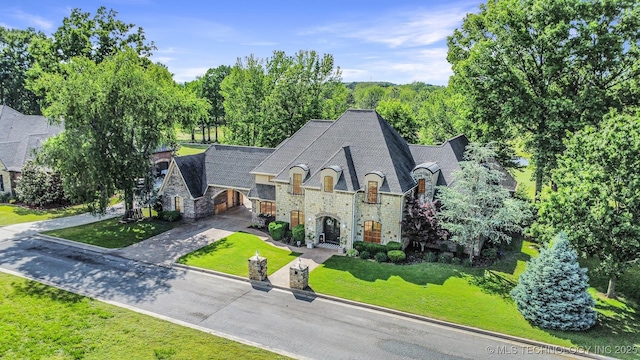 french country home with stone siding, driveway, and a front lawn