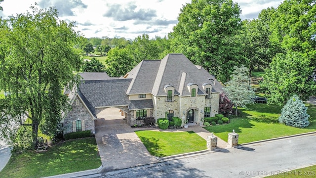 french country style house featuring stone siding, a front lawn, and concrete driveway