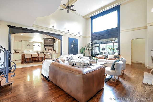 living area with arched walkways, high vaulted ceiling, a ceiling fan, light wood-type flooring, and baseboards