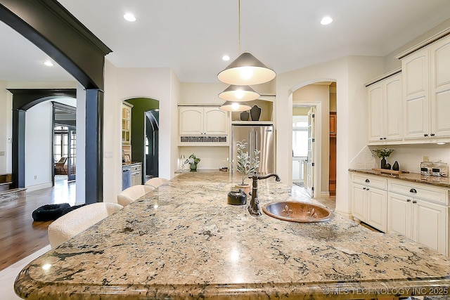 kitchen with high quality fridge, arched walkways, a sink, light stone counters, and recessed lighting