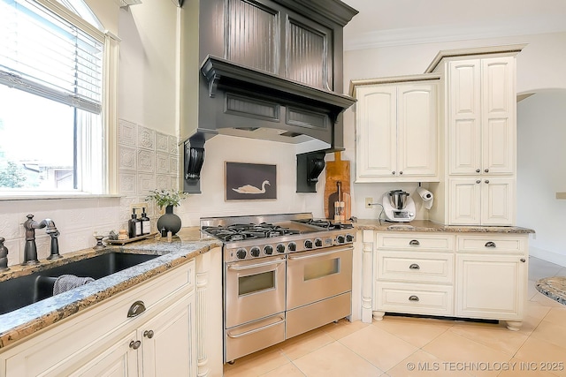kitchen with double oven range, a sink, light tile patterned floors, ornamental molding, and light stone countertops
