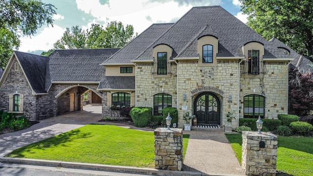 french country inspired facade featuring stone siding, french doors, and a front yard