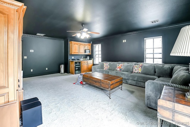living room with crown molding, light carpet, a ceiling fan, bar area, and wine cooler