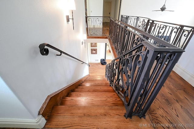 staircase with wood finished floors, baseboards, and ceiling fan