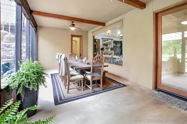 dining room with beamed ceiling, healthy amount of natural light, concrete flooring, and a ceiling fan
