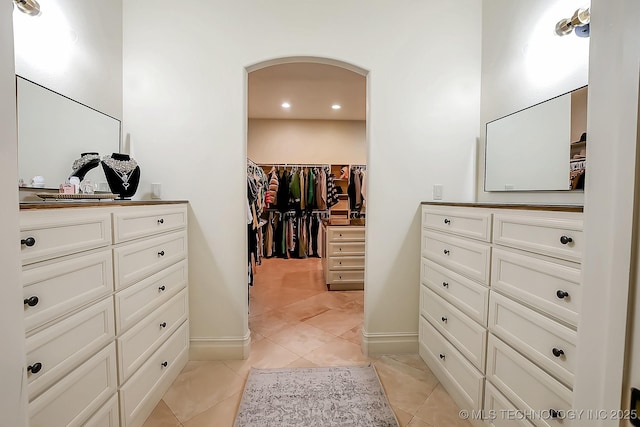 spacious closet with arched walkways and light tile patterned floors