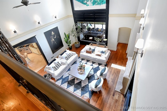 living area featuring a towering ceiling, arched walkways, wood finished floors, ceiling fan, and baseboards