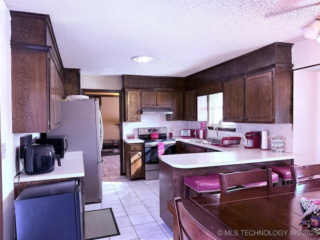 2902 Hilltop Ave, Muskogee, OK 74403 - kitchen with electric stove, under cabinet range hood, a peninsula, a textured ceiling, and light countertops
