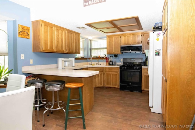 kitchen featuring black gas range oven, freestanding refrigerator, ventilation hood, a peninsula, and dark wood-style flooring
