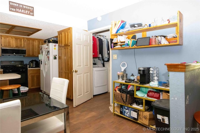 kitchen featuring black range with gas cooktop, washer / clothes dryer, white refrigerator with ice dispenser, stainless steel microwave, and wood finished floors
