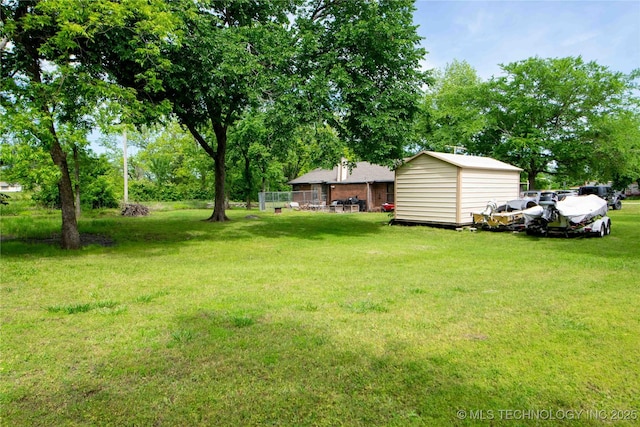 view of grassy yard with a storage shed, an outbuilding, and view of wooded area
