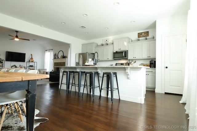 118 W 130th Pl S, Jenks, OK 74037 - kitchen with appliances with stainless steel finishes, a breakfast bar area, ceiling fan, dark wood-type flooring, and an island with sink