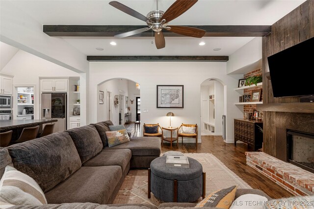 2835 E 104th St, Tulsa, OK 74137 - living room with arched walkways, beam ceiling, a brick fireplace, wood finished floors, and ceiling fan