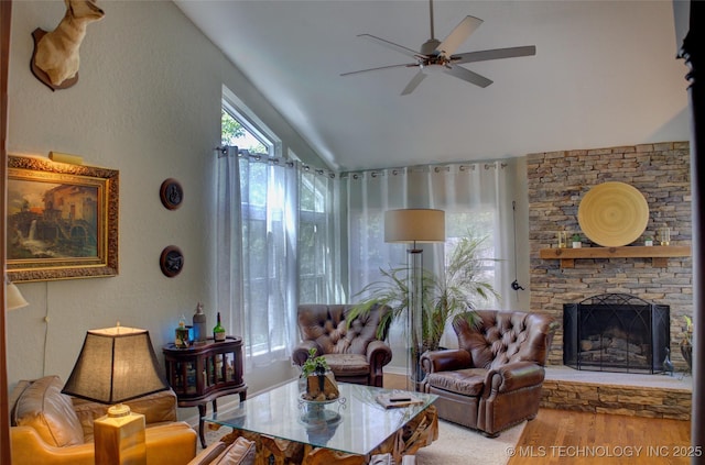 living area featuring vaulted ceiling, wood finished floors, ceiling fan, and a fireplace