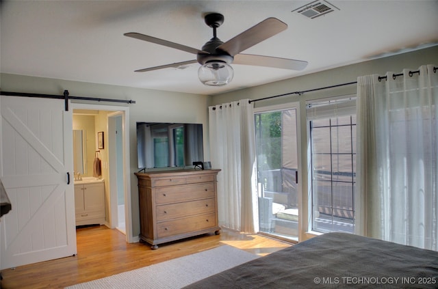 bedroom with light wood-type flooring, access to outside, a barn door, ensuite bathroom, and ceiling fan