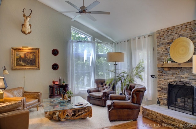 living area with lofted ceiling, a ceiling fan, wood finished floors, and a stone fireplace
