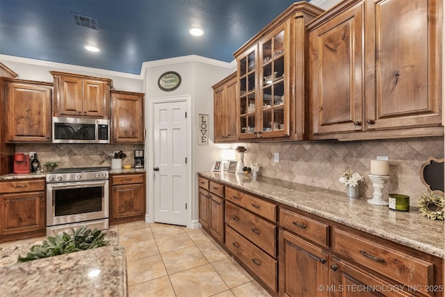 7333 S 286th E Ave, Broken Arrow, OK 74014 - kitchen featuring appliances with stainless steel finishes, backsplash, brown cabinets, light stone counters, and glass insert cabinets