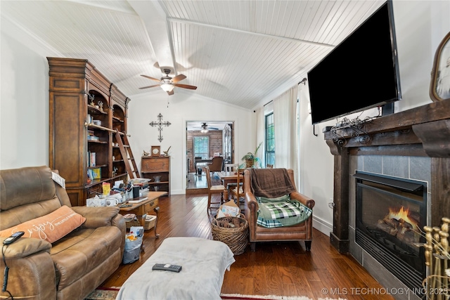 living area featuring ceiling fan, a tiled fireplace, dark wood finished floors, vaulted ceiling, and baseboards
