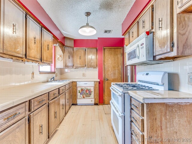 205 Lester Ln, Cleveland, OK 74020 - kitchen featuring white appliances, a sink, decorative backsplash, tile counters, and light wood finished floors